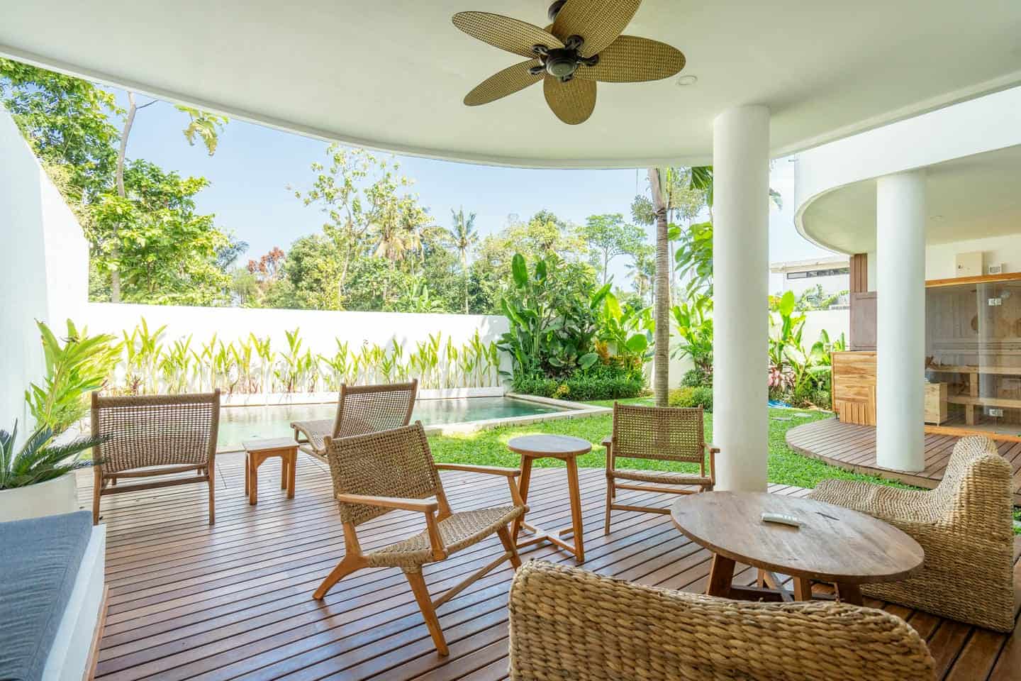 Outdoor patio with chairs, ceiling fan, and greenery.