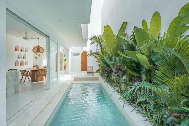 Modern indoor pool with lush plants and dining area.
