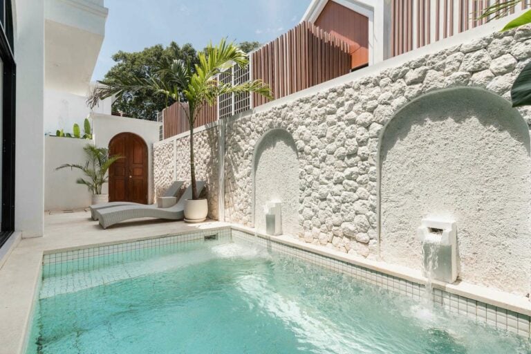 Sunny patio with pool and stone wall fountain.