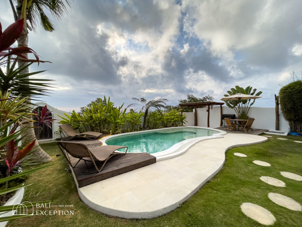 Tropical backyard with pool and lounge chairs.