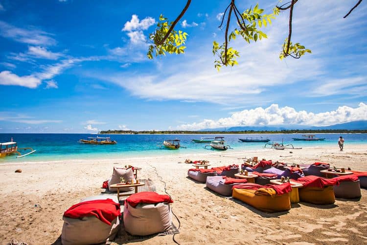 Tropical beach with boats and colorful loungers.