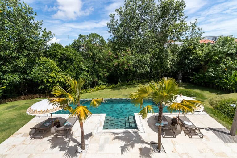 Outdoor pool area with sun loungers and palm trees.