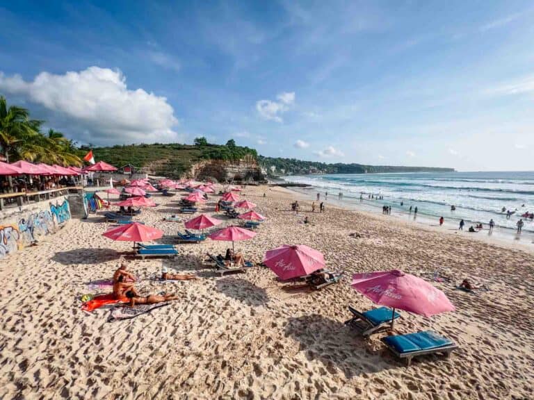 Crowded beach with pink umbrellas and lounge chairs.