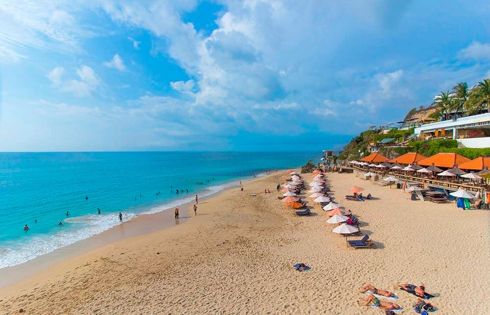 Sunny beach with umbrellas and people swimming.