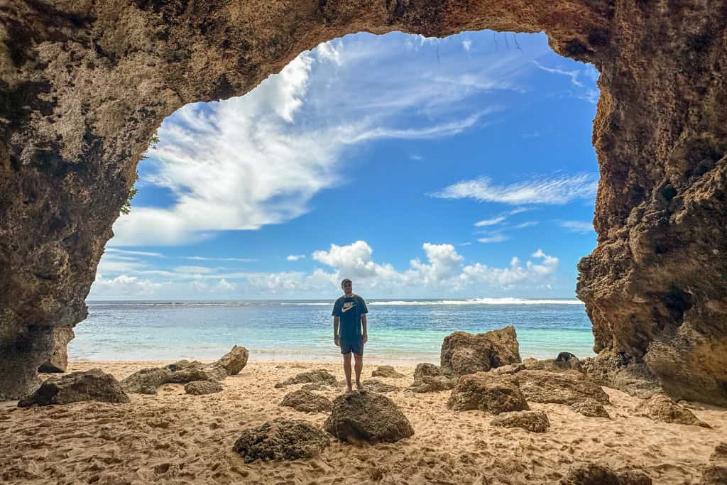 Person stands on beach under rocky archway