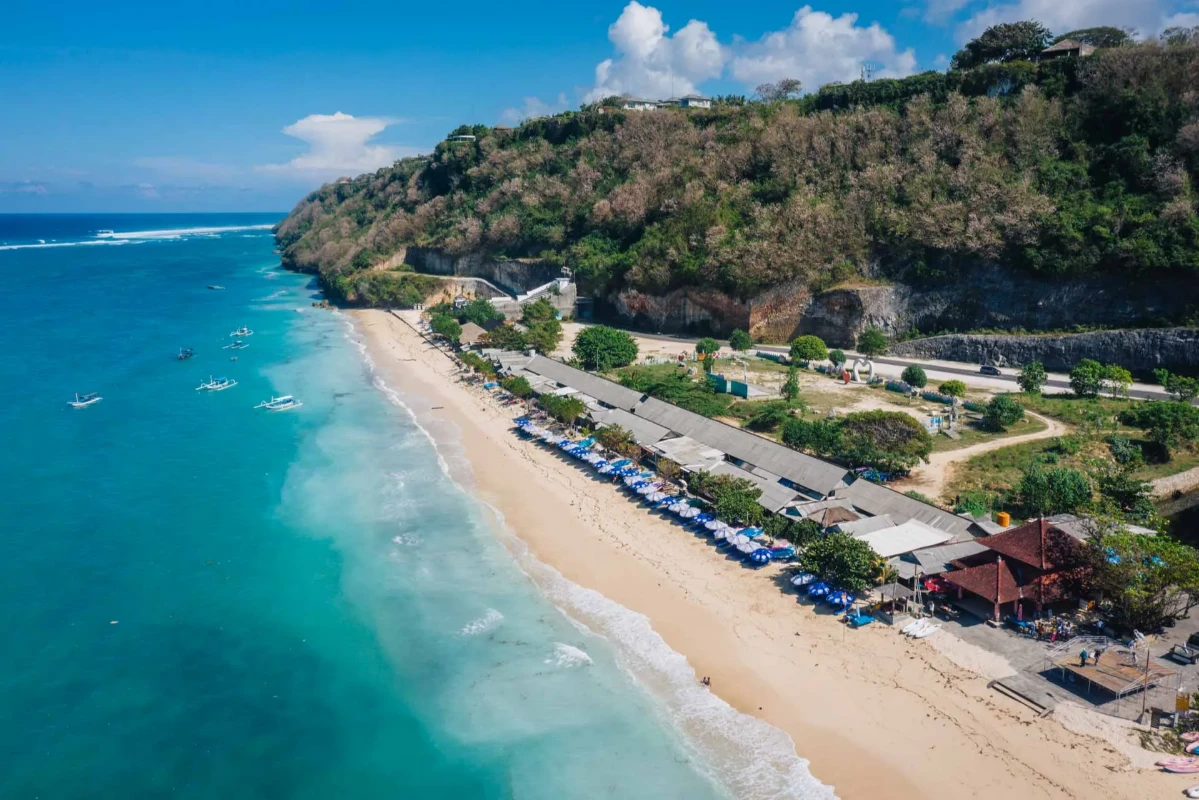 Beautiful beach with blue umbrellas and lush cliffs.