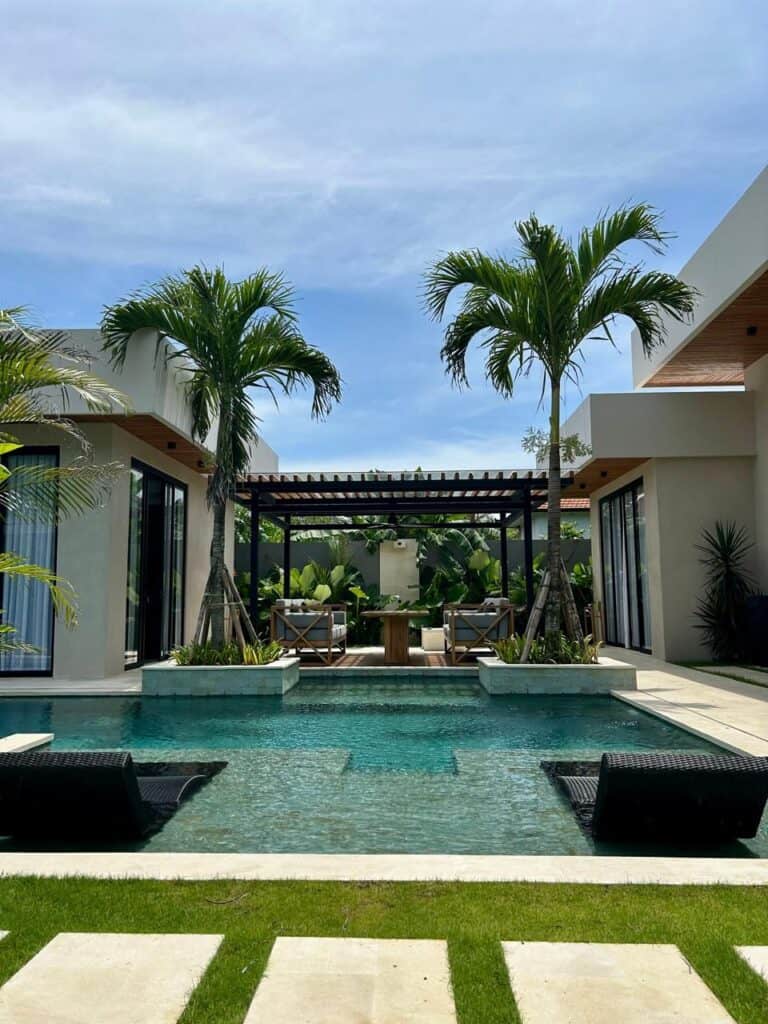 Luxury villa pool with palm trees and lounge chairs.