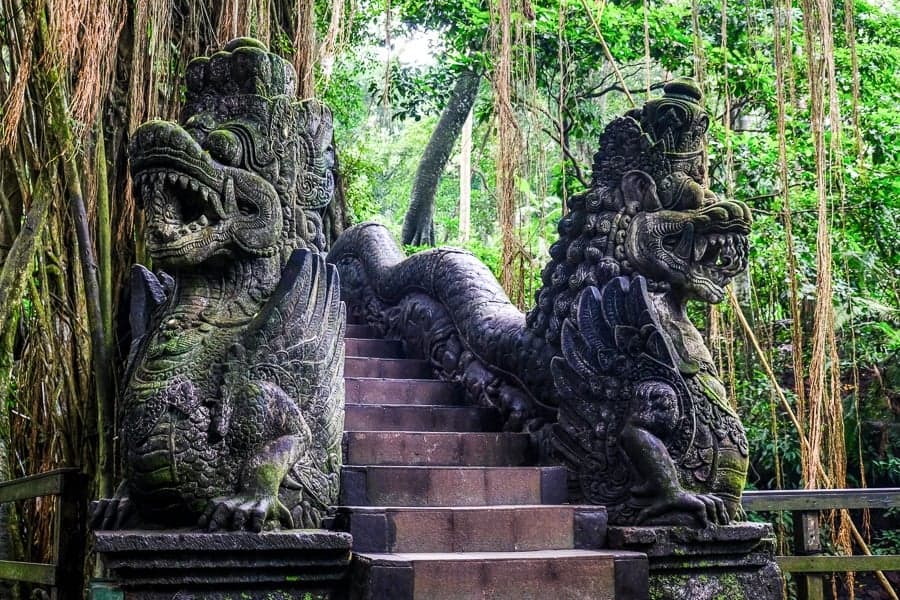 Balinese stone dragon statues in lush forest setting.