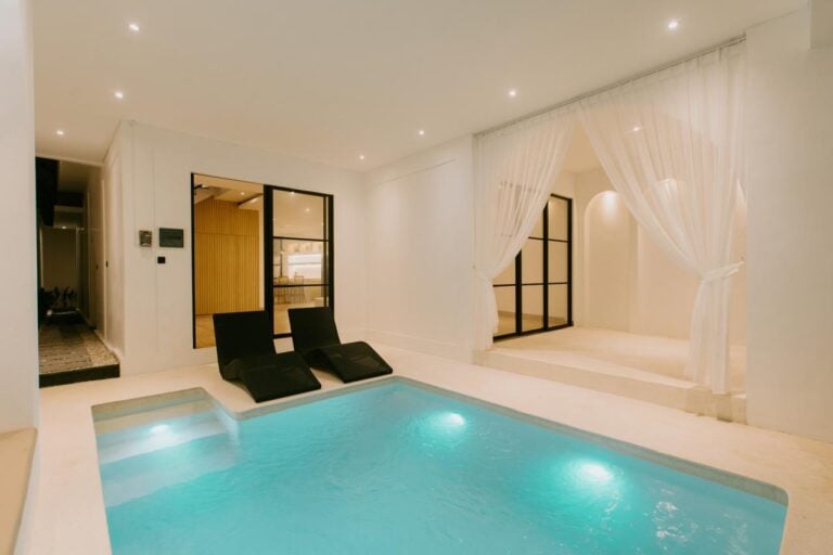 Modern indoor pool with lounge chairs and curtains.