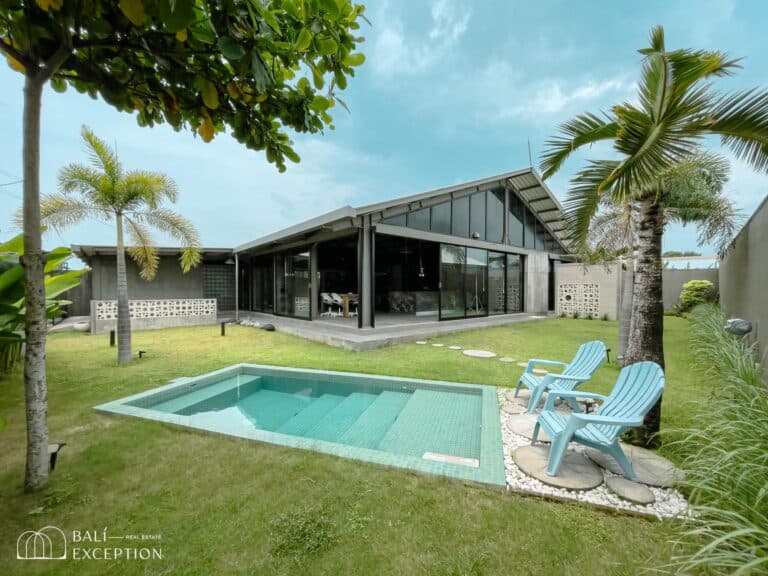 Modern glass house with pool and patio chairs.