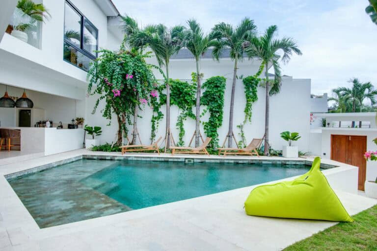 Modern outdoor pool with tropical plants and deck chairs.