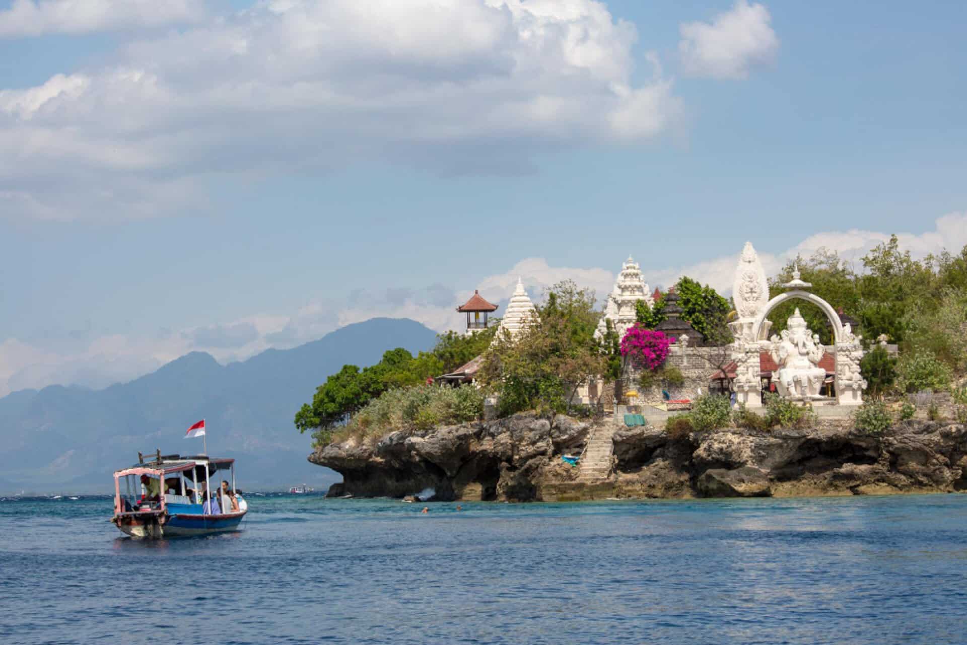 Boat beside Balinese temple on rocky coastline.