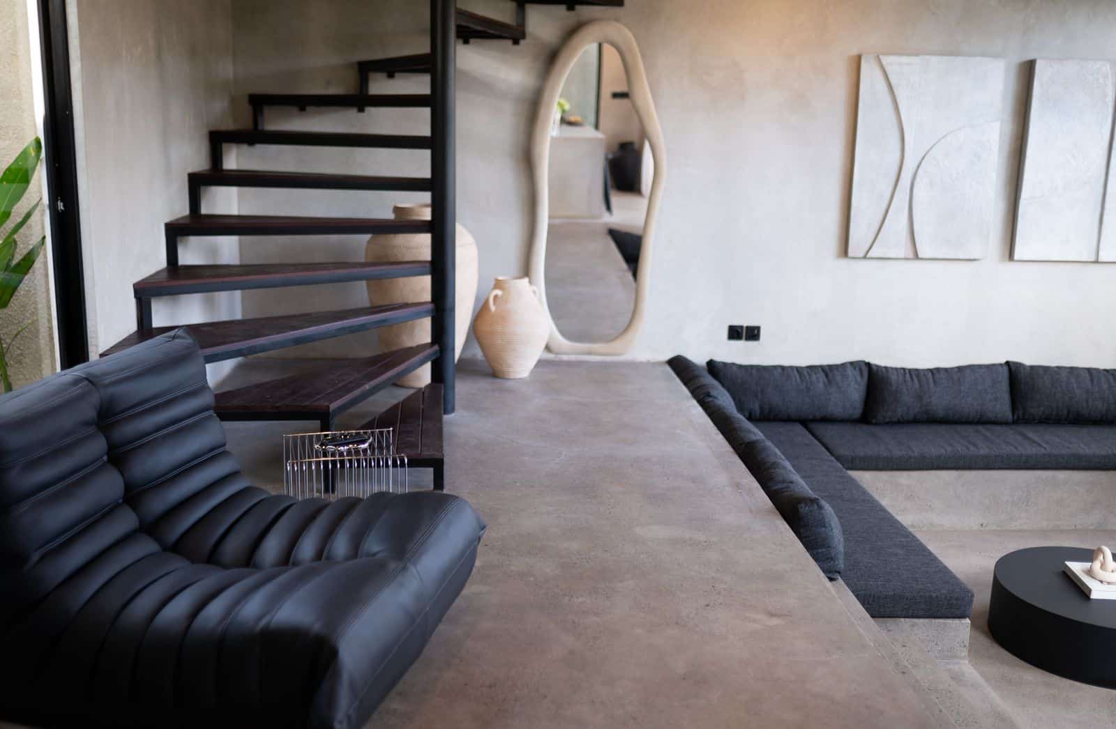 Modern living room with black furniture and staircase.