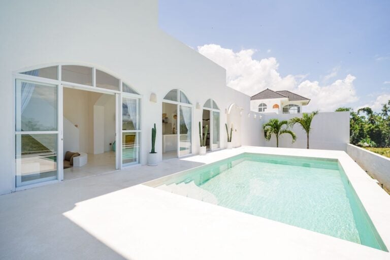 Modern white villa with pool and palm trees.